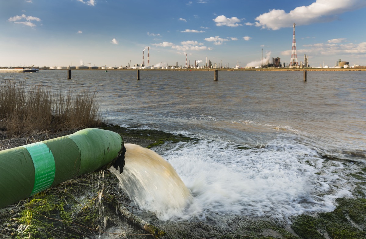 A wastewater pipe and a large oil refinery in the harbor of Antwerp, Belgium with blue sky and warm evening light.